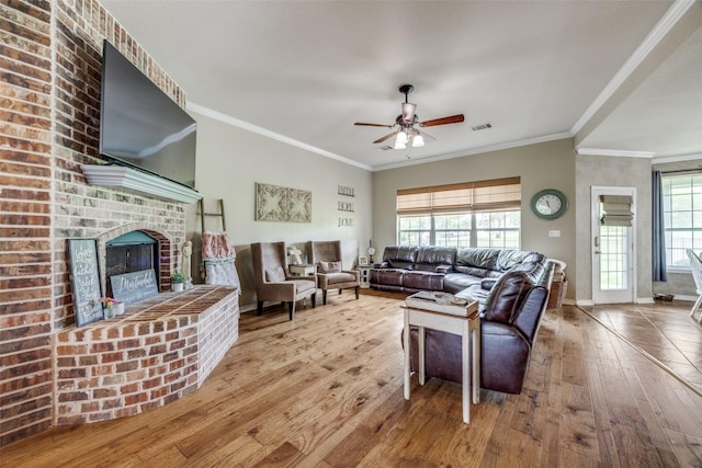 living area with hardwood / wood-style floors, ornamental molding, ceiling fan, a brick fireplace, and visible vents