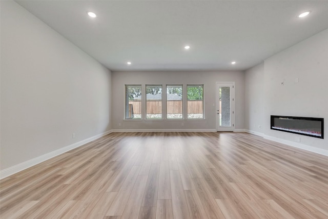 unfurnished living room featuring baseboards, recessed lighting, light wood-style floors, and a glass covered fireplace
