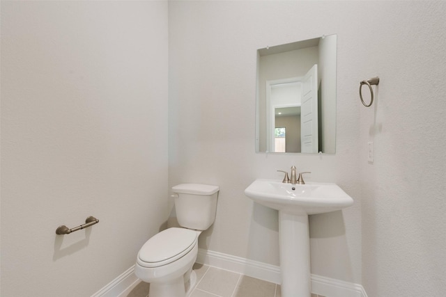 half bathroom with toilet, a sink, tile patterned floors, and baseboards
