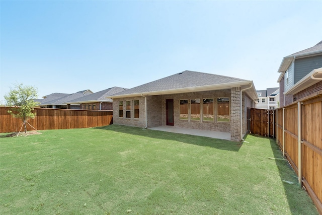 back of house featuring brick siding, a fenced backyard, a shingled roof, and a yard