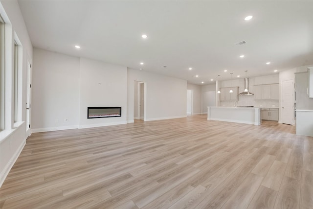 unfurnished living room featuring recessed lighting, visible vents, a glass covered fireplace, and light wood-type flooring