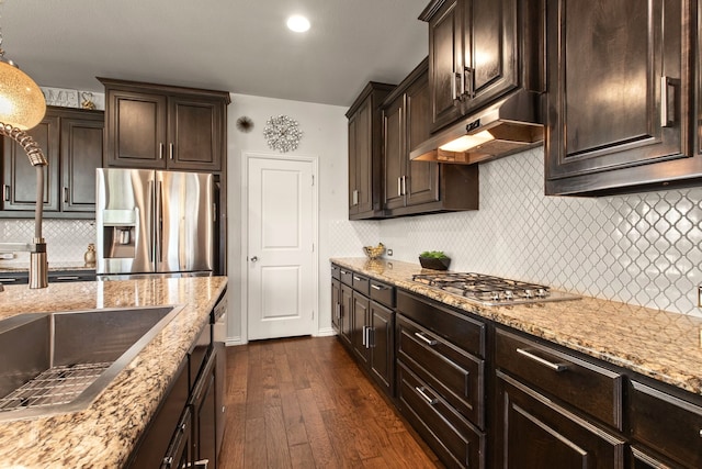 kitchen featuring under cabinet range hood, tasteful backsplash, dark wood-type flooring, dark brown cabinetry, and appliances with stainless steel finishes