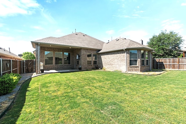 rear view of property featuring brick siding, a fenced backyard, a patio area, and a lawn