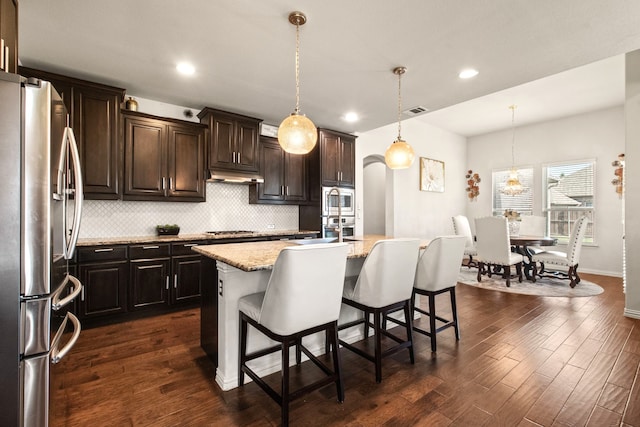 kitchen featuring light stone countertops, stainless steel appliances, tasteful backsplash, dark wood-type flooring, and visible vents