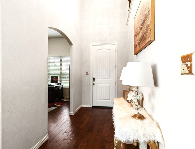 foyer entrance featuring a towering ceiling, arched walkways, dark wood-style flooring, and baseboards