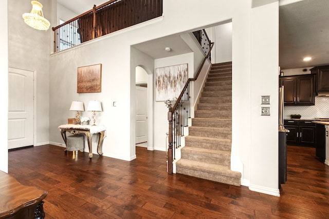 staircase with a towering ceiling, wood finished floors, baseboards, and arched walkways