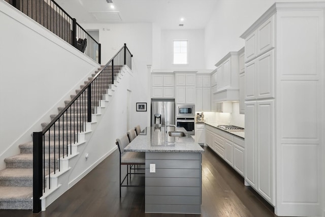 kitchen with light stone counters, appliances with stainless steel finishes, white cabinets, dark wood-style flooring, and a towering ceiling