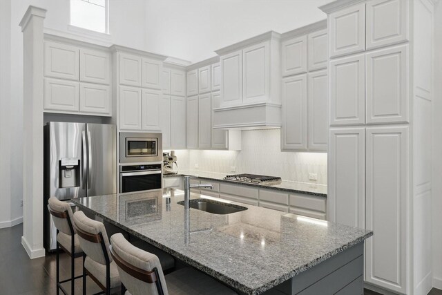 kitchen featuring appliances with stainless steel finishes, light stone counters, white cabinets, and a sink