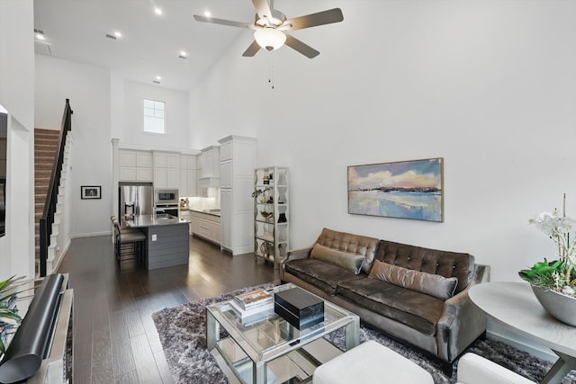 living room featuring dark wood-style flooring, stairway, high vaulted ceiling, ceiling fan, and baseboards