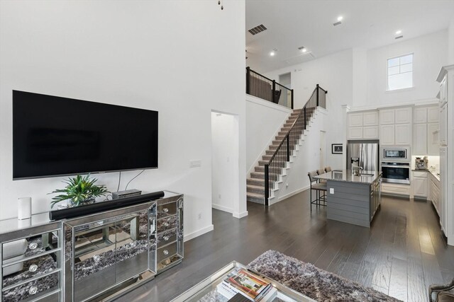 living area with stairway, visible vents, dark wood-type flooring, baseboards, and a towering ceiling