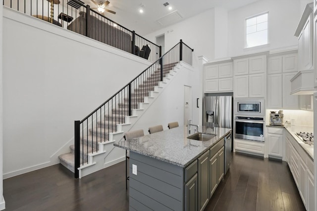 kitchen featuring a high ceiling, a sink, gray cabinets, appliances with stainless steel finishes, and dark wood finished floors