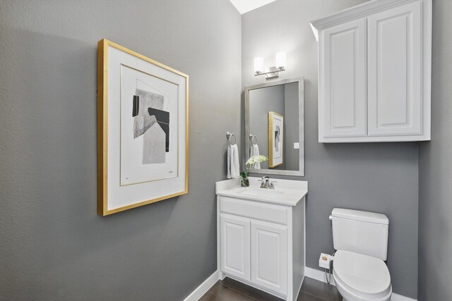 half bath featuring baseboards, toilet, and vanity