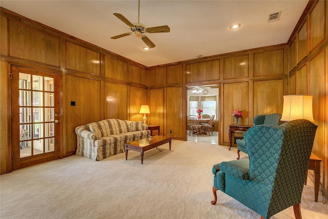 living room featuring wood walls, light colored carpet, visible vents, and a ceiling fan