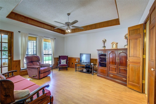 interior space with a ceiling fan, a wainscoted wall, a textured ceiling, and light wood-style flooring