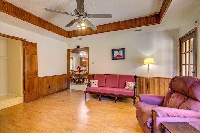 living room featuring light wood-style floors, ceiling fan, wooden walls, visible vents, and a textured ceiling