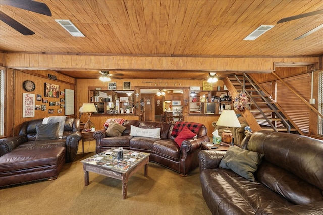 carpeted living area with wooden ceiling, stairway, ceiling fan, visible vents, and wood walls