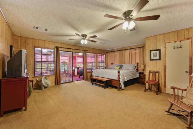 bedroom with wood walls, a textured ceiling, visible vents, and light carpet
