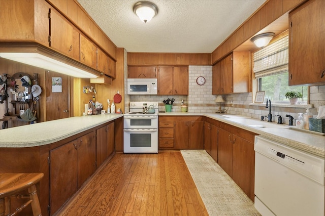 kitchen with brown cabinetry, a textured ceiling, a sink, and white appliances