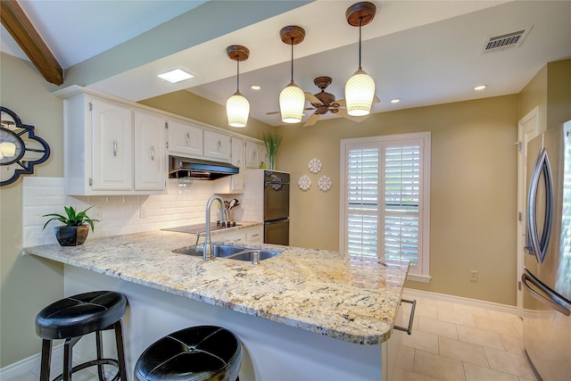 kitchen featuring a sink, under cabinet range hood, dobule oven black, a peninsula, and freestanding refrigerator