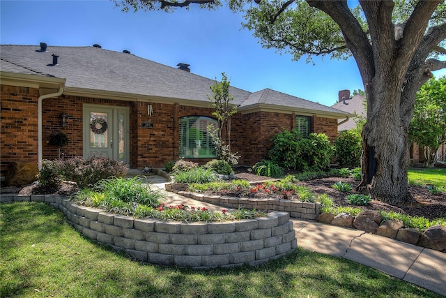 ranch-style home with a chimney, brick siding, and roof with shingles