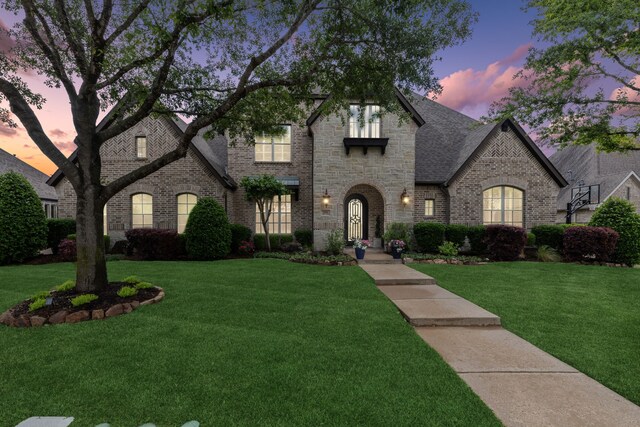 french country style house with brick siding, a front yard, and stone siding