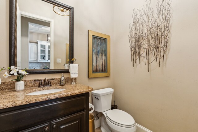 half bathroom featuring toilet, vanity, and baseboards