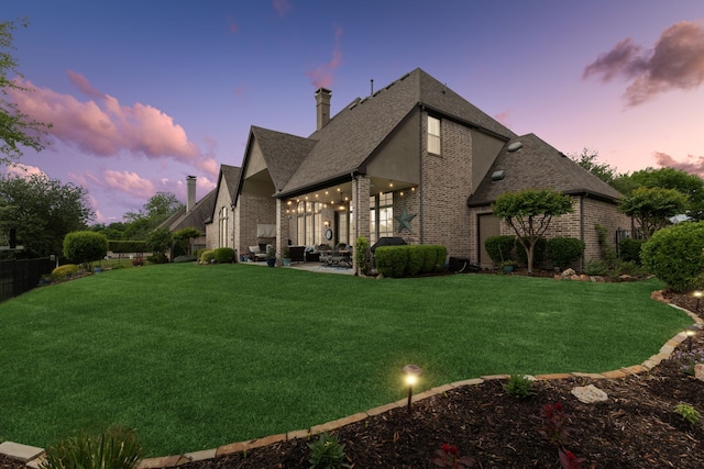 back of property featuring a lawn, a patio area, and brick siding