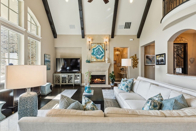 living room featuring wood finished floors, a fireplace, beam ceiling, visible vents, and high vaulted ceiling