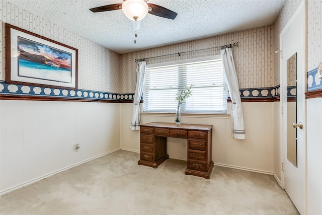 unfurnished office featuring light carpet, a textured ceiling, a ceiling fan, wallpapered walls, and baseboards