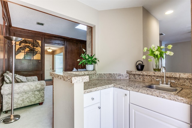 kitchen featuring a sink, a peninsula, light countertops, white cabinetry, and recessed lighting