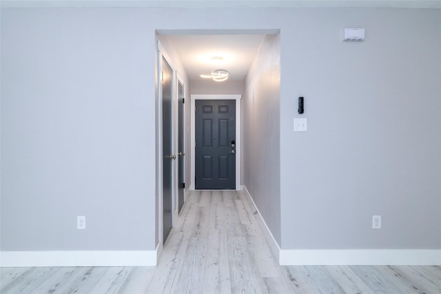 corridor with light wood-type flooring and baseboards