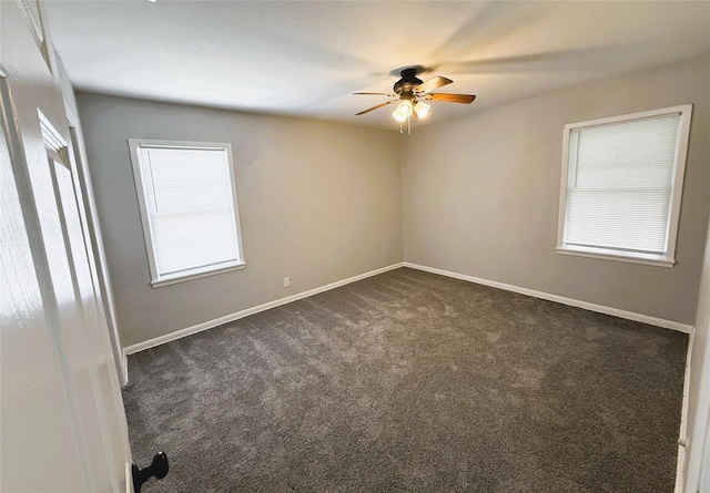 empty room with baseboards, dark carpet, and a ceiling fan