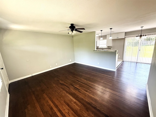 unfurnished living room featuring dark wood-type flooring, baseboards, and ceiling fan with notable chandelier