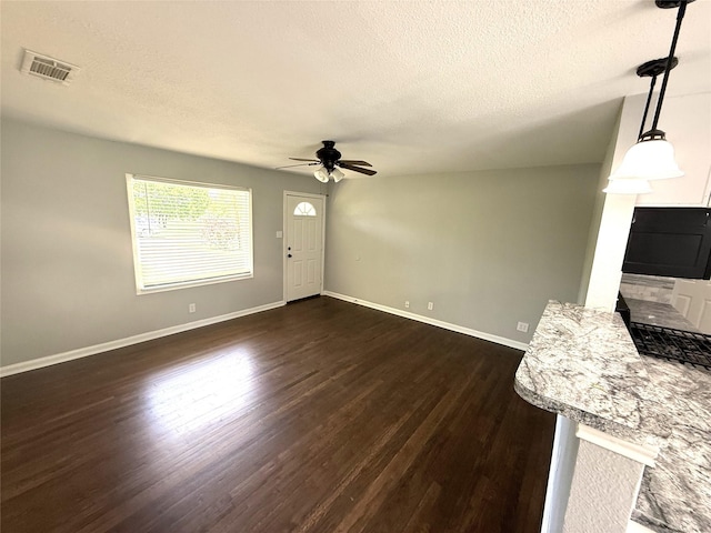 unfurnished living room featuring dark wood-style flooring, visible vents, a ceiling fan, and a textured ceiling