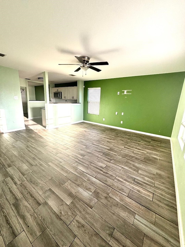 unfurnished living room with baseboards, wood finished floors, ceiling fan, and plenty of natural light