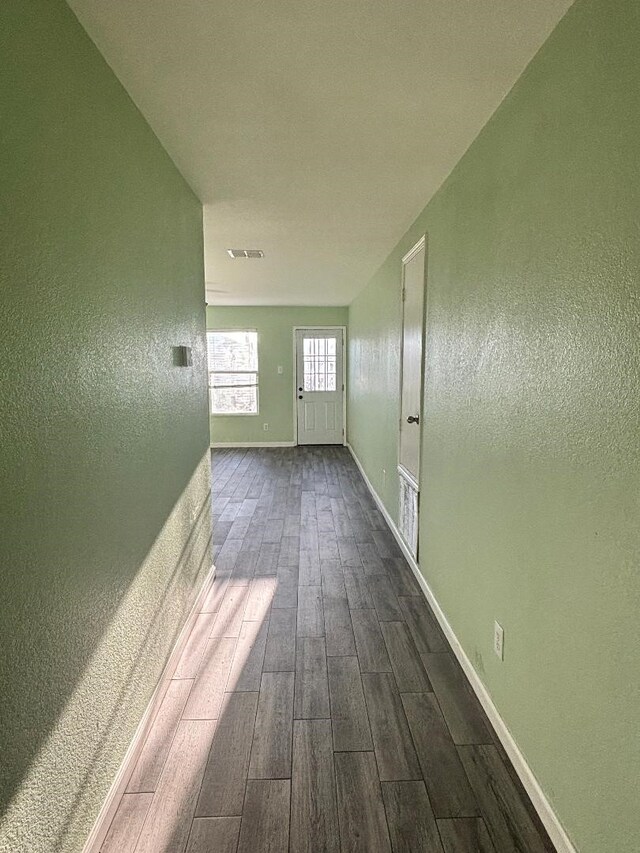 hallway with baseboards, visible vents, dark wood-type flooring, and a textured wall