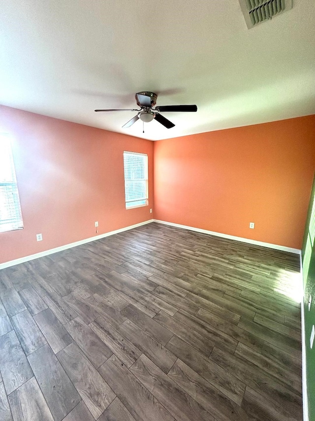 unfurnished room with baseboards, visible vents, a ceiling fan, and dark wood-style flooring