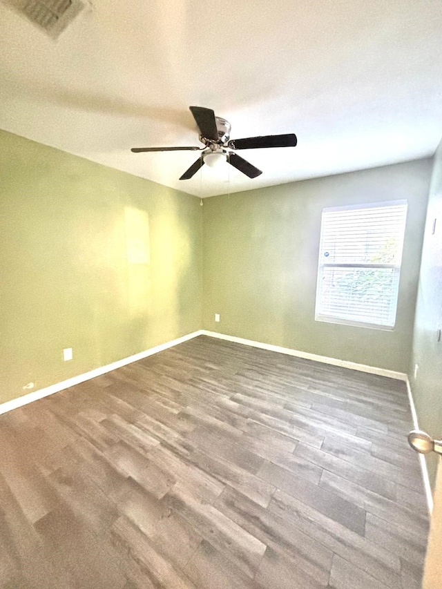 spare room featuring wood finished floors, visible vents, a ceiling fan, and baseboards