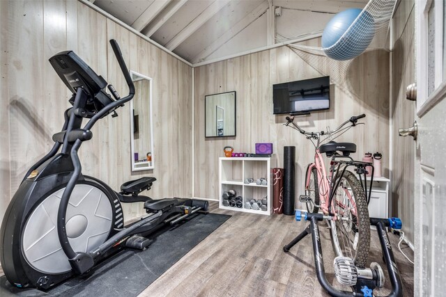 exercise area with lofted ceiling, wooden walls, and wood finished floors