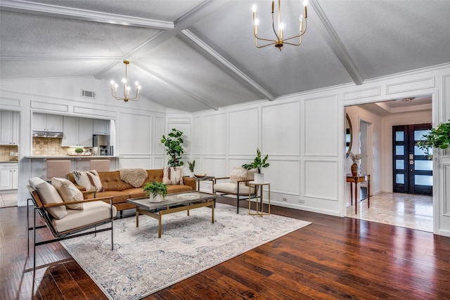 living area with dark wood-style floors, visible vents, a notable chandelier, and a decorative wall