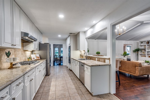 kitchen featuring white cabinetry, tasteful backsplash, a sink, appliances with stainless steel finishes, and under cabinet range hood