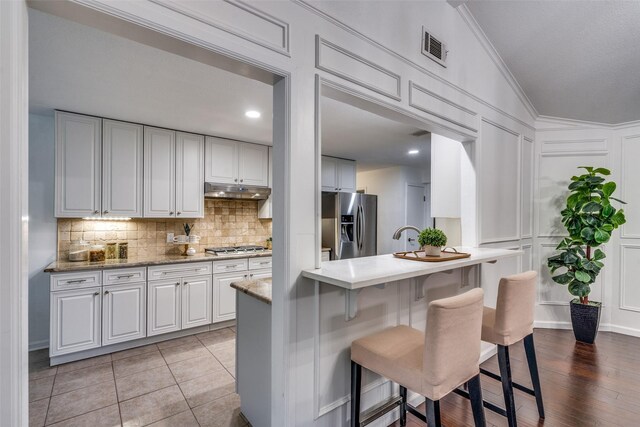 kitchen featuring stainless steel appliances, a breakfast bar area, backsplash, a decorative wall, and white cabinetry