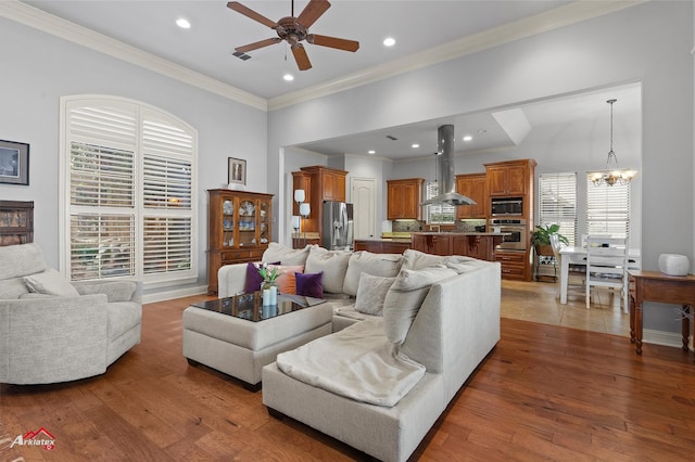living area featuring visible vents, ornamental molding, ceiling fan with notable chandelier, and wood finished floors