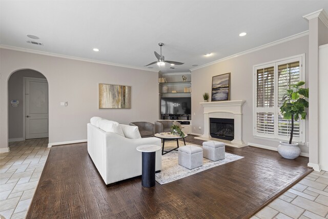 living area featuring baseboards, arched walkways, a ceiling fan, and ornamental molding