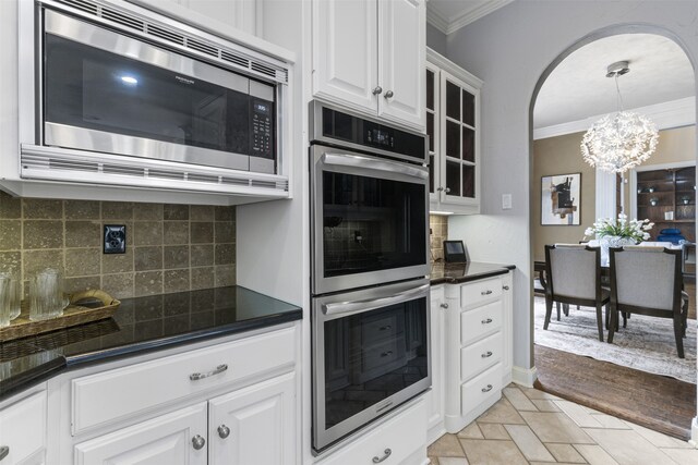 kitchen with dark countertops, appliances with stainless steel finishes, ornamental molding, and a notable chandelier