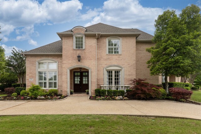 french provincial home with brick siding, a front lawn, roof with shingles, and french doors