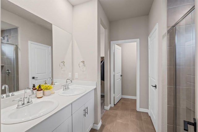 full bath with baseboards, a shower stall, double vanity, and a sink