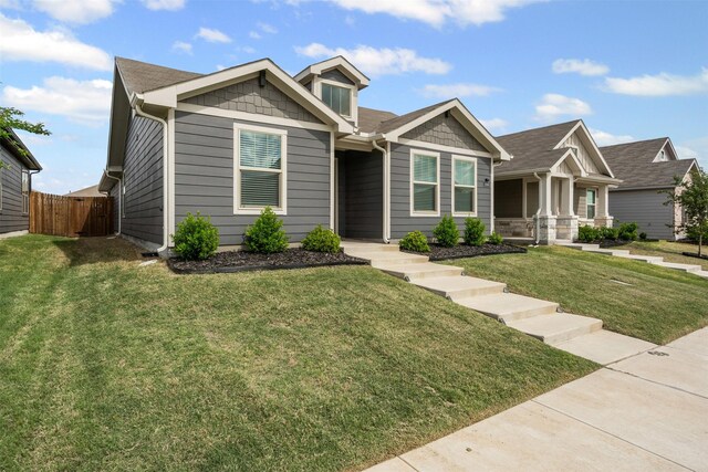 view of front facade with fence, roof with shingles, and a front lawn