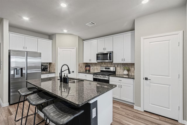 kitchen with light wood finished floors, a sink, stainless steel appliances, visible vents, and backsplash