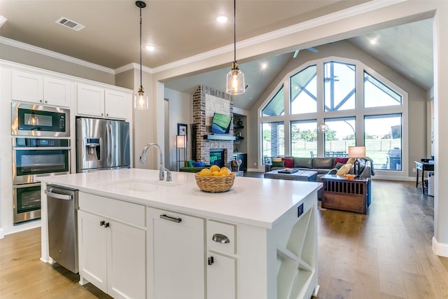 12492 Palmer Dr, Fort Worth, TX 76179 - kitchen with white cabinets, a sink, a brick fireplace, an island with sink, and stainless steel appliances